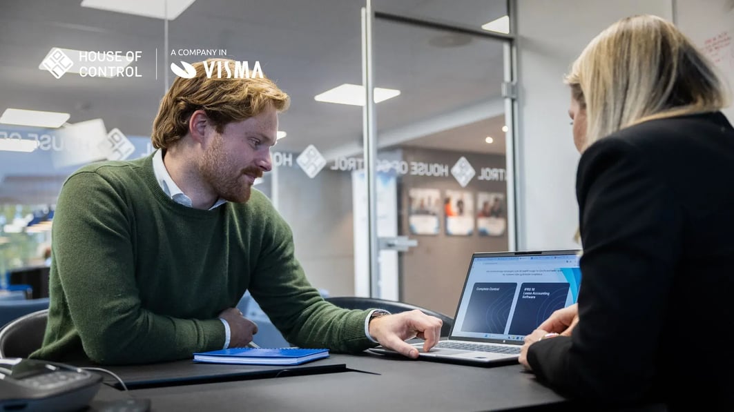 A man in a green jumper showing a woman a presentation slide on the computer