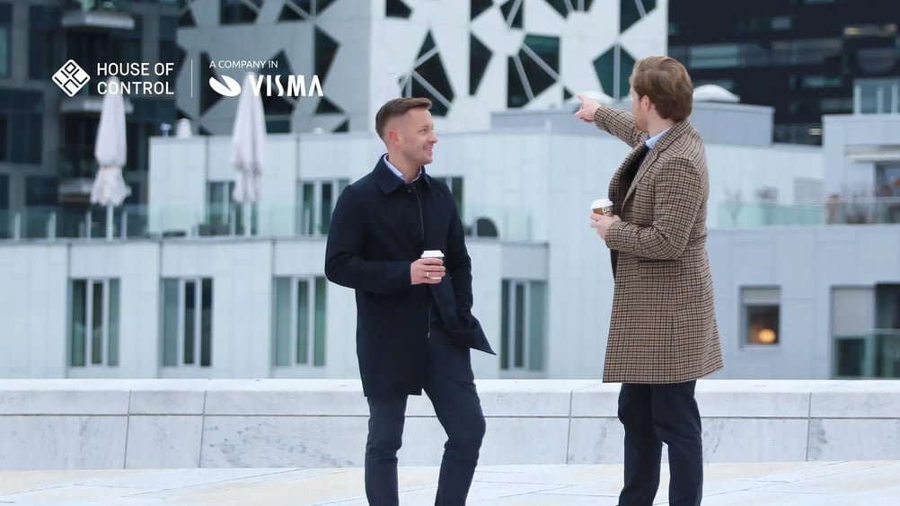 Two men in the city, one is pointing at the buildings in the background