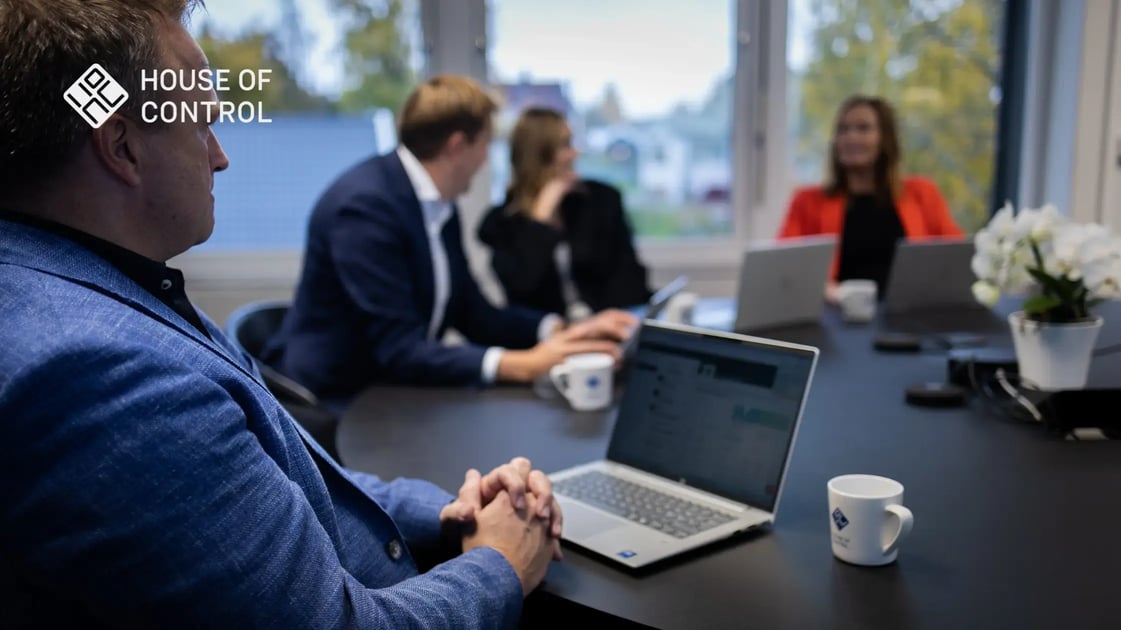 A man in a blue suit sits with his hands folded in front of the computer in a meeting