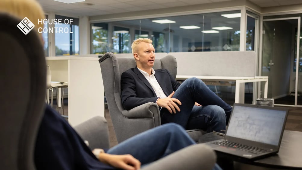 A blonde man is sitting with his legs crossed in a chair, looking like he's in a conversation at the office