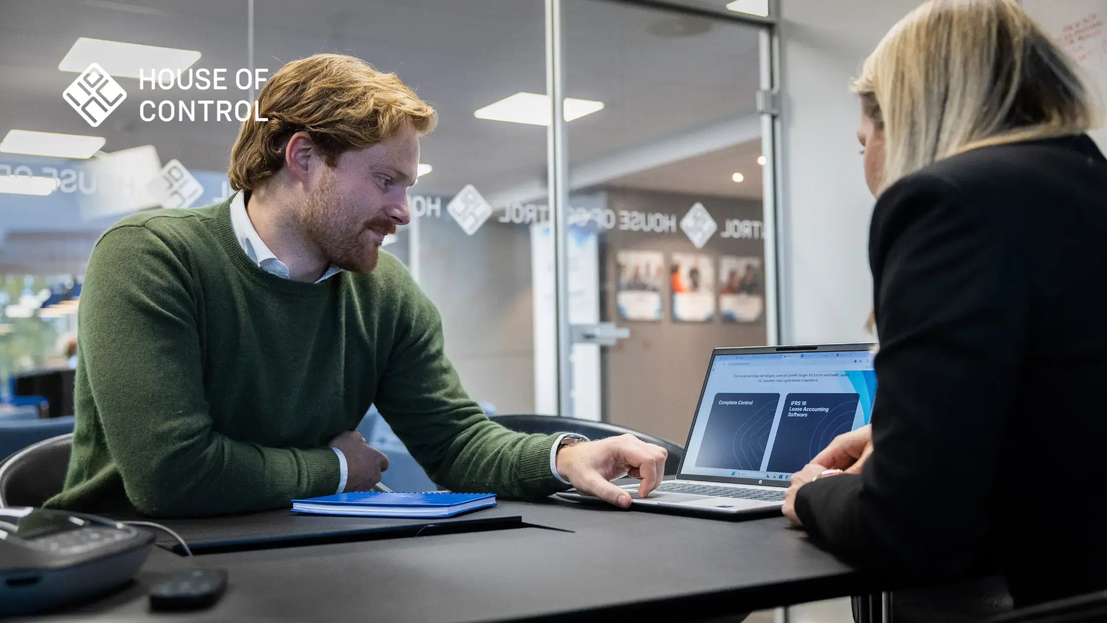 Mann i grønn genser som ser på en PC-skjerm med en kollega