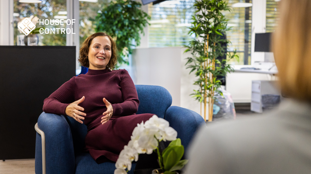 En glad kvinne sitter i en blå lenestol og gestikulerer engasjert mens hun samtaler med en person. House of Control-logoen vises i høyre hjørne, og stemningen er profesjonell og imøtekommende.