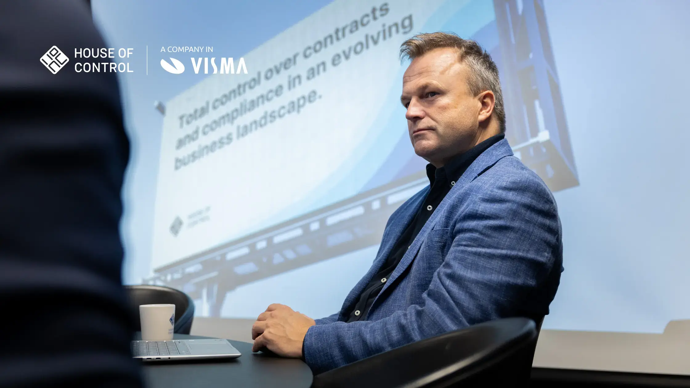 A man is sitting in a meeting in front of a presentation on a big screen
