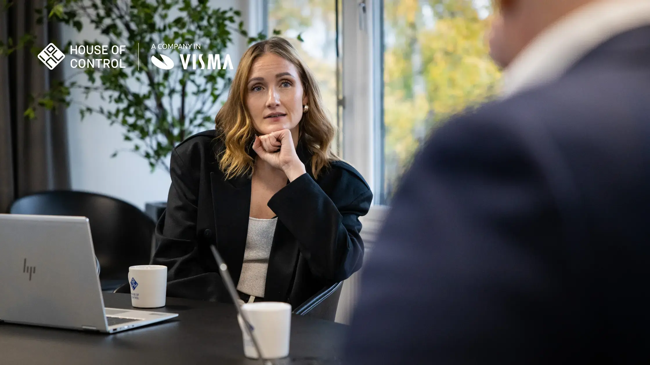 A woman in a black blazer is sitting in a meeting looking concentrated