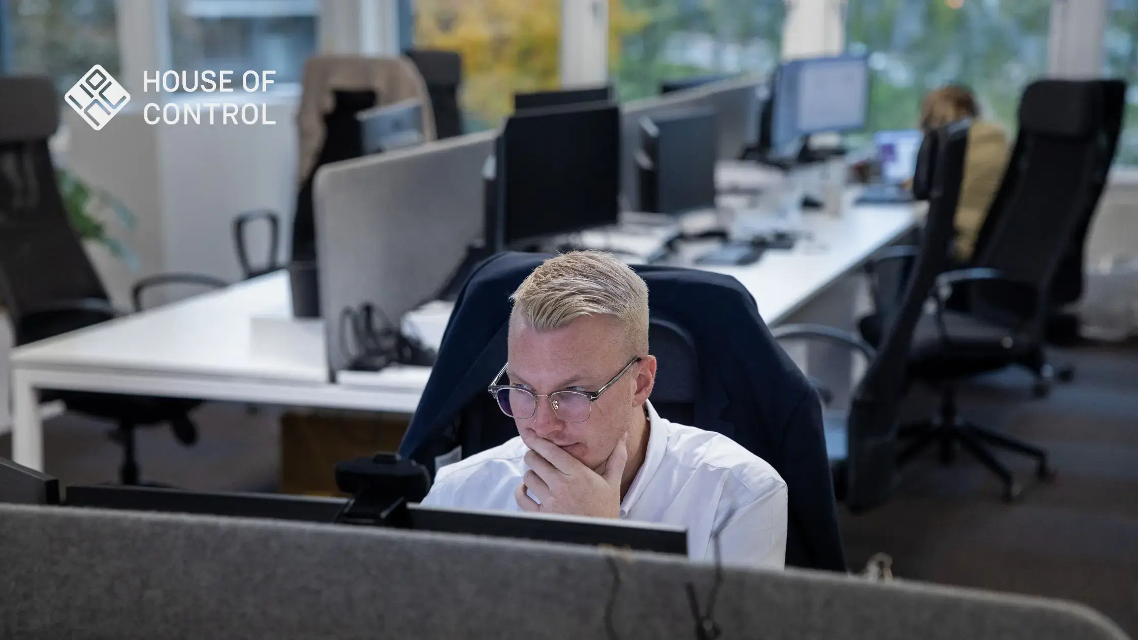 A blonde man is sitting in front of the computer at the office looking concentrated