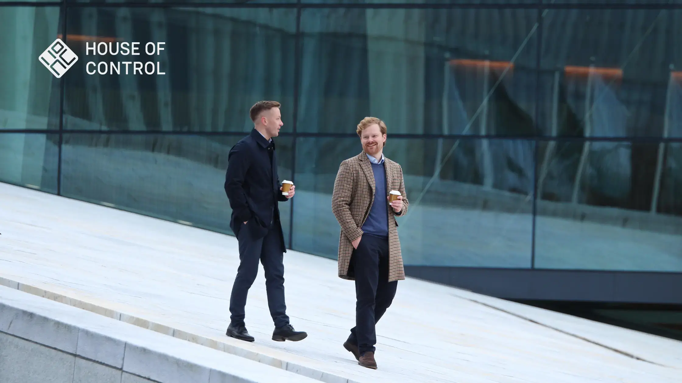 Two men walking on top of Oslo Opera House with coffees in their hand and smiling