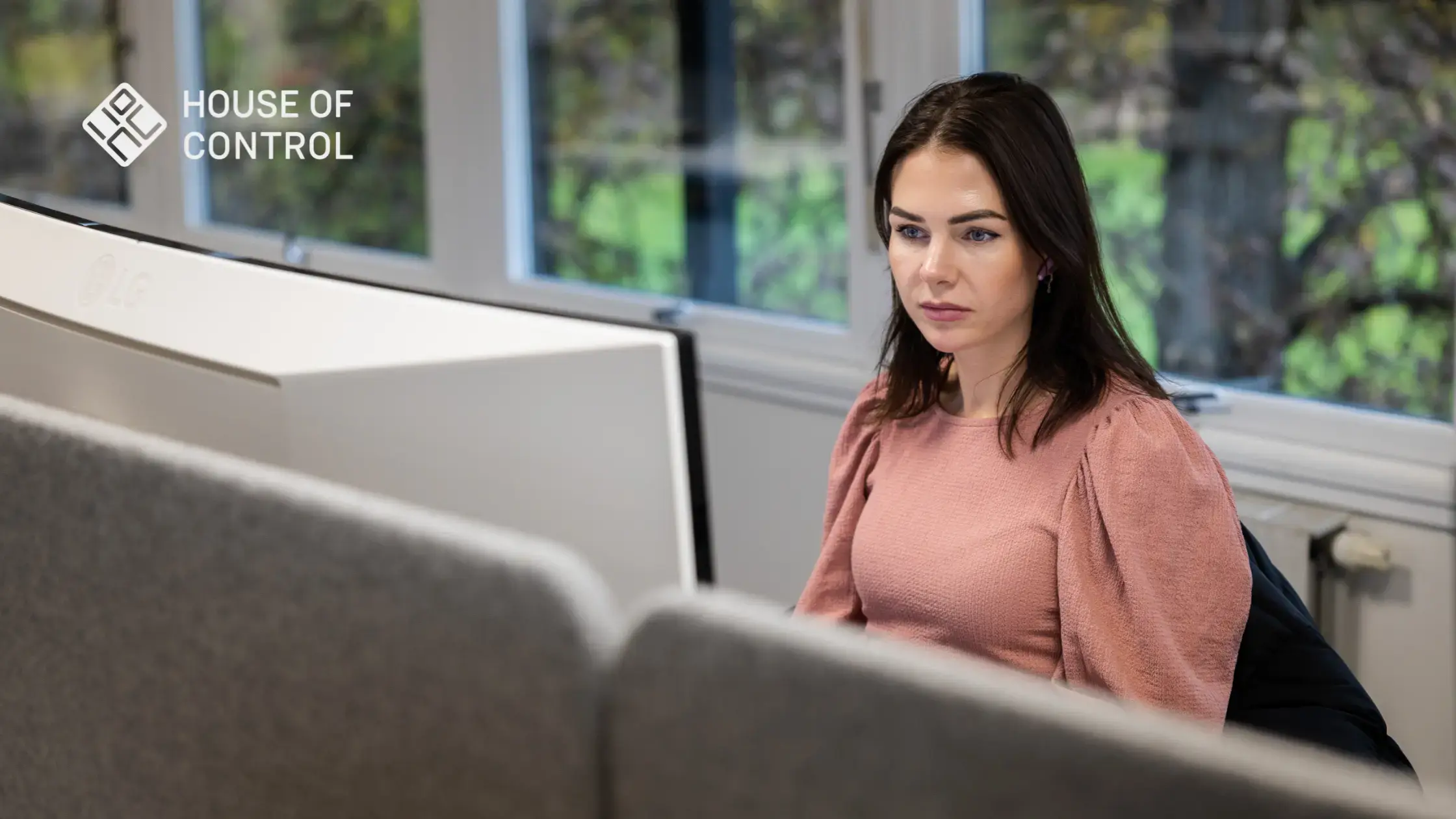 A focused employee at house of Control working at her desk while sitting down, looking at her screen