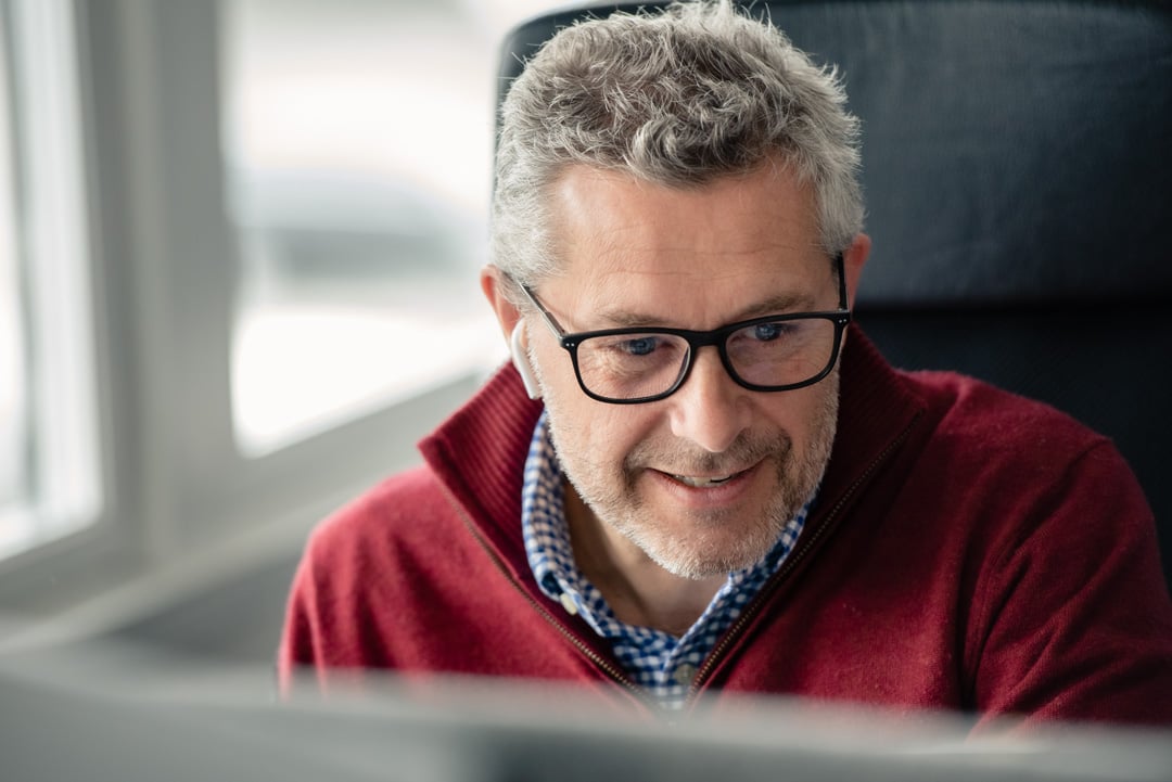 En smilende mann med briller som ser på en PC-skjerm på et kontor